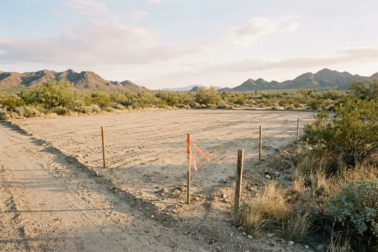 A cleared and graded desert building lot marked with wooden survey stakes